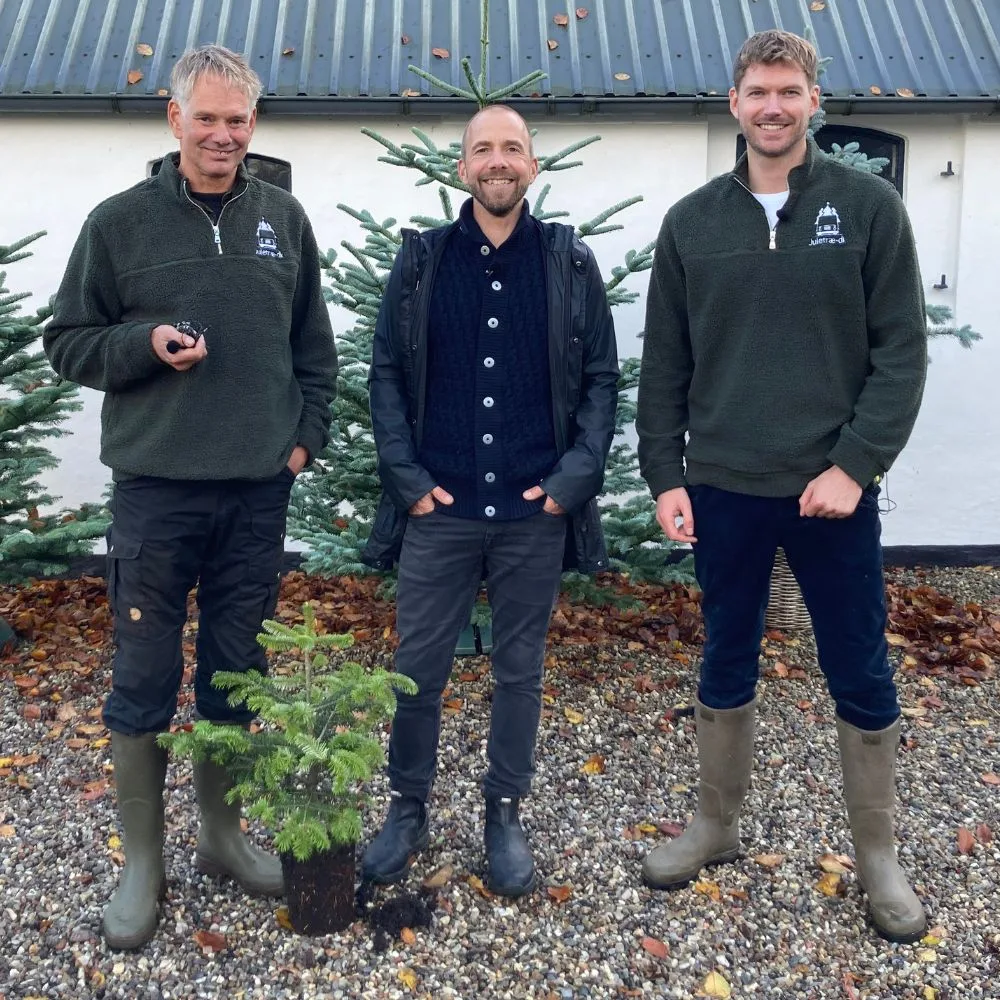 Søren vester på besøg i juletræerne Tre mænd står foran en bygning iført arbejdstøj og gummistøvler