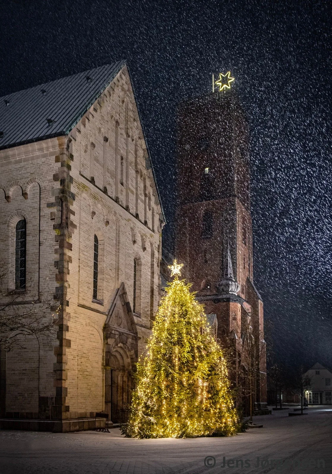 be6ac5f1ec144c7e3199eff813c81e1d Oplyst juletræ foran kirke i snevejr