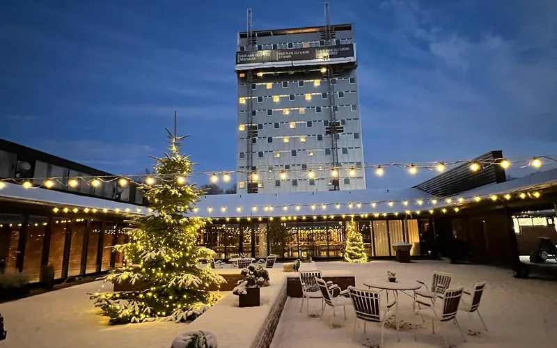 fa2bb206d3a926aef61b69a840001cfa Pyntet juletræ i gårdmiljø med lyskæder og hotel i baggrunden